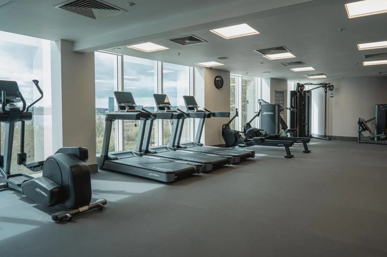 a gym with treadmills and ellipticals in a room with windows at voco St. David's Cardiff by IHG in Cardiff
