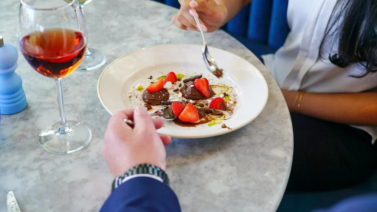 a person eating a plate of food with a glass of wine at voco St. David's Cardiff by IHG in Cardiff